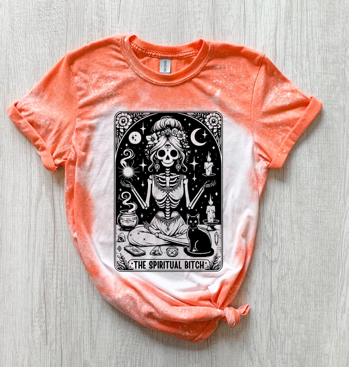 A bleached orange  t-shirt with a black and white illustration of a skeleton woman with a cat and the text "The Spiritual Bitch".