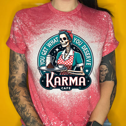 A red t-shirt with a bleached design featuring a skeleton wearing a red and white dress and holding a tray with a cup of coffee and a piece of cake. The text "You get what you deserve" is written around the skeleton. Below the skeleton is the text "Karma Cafe".