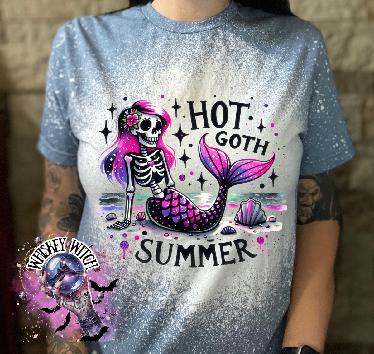 An indigo blue  t-shirt with a bleach-splattered design featuring a pink and purple skeleton mermaid with the text "Hot Goth Summer".