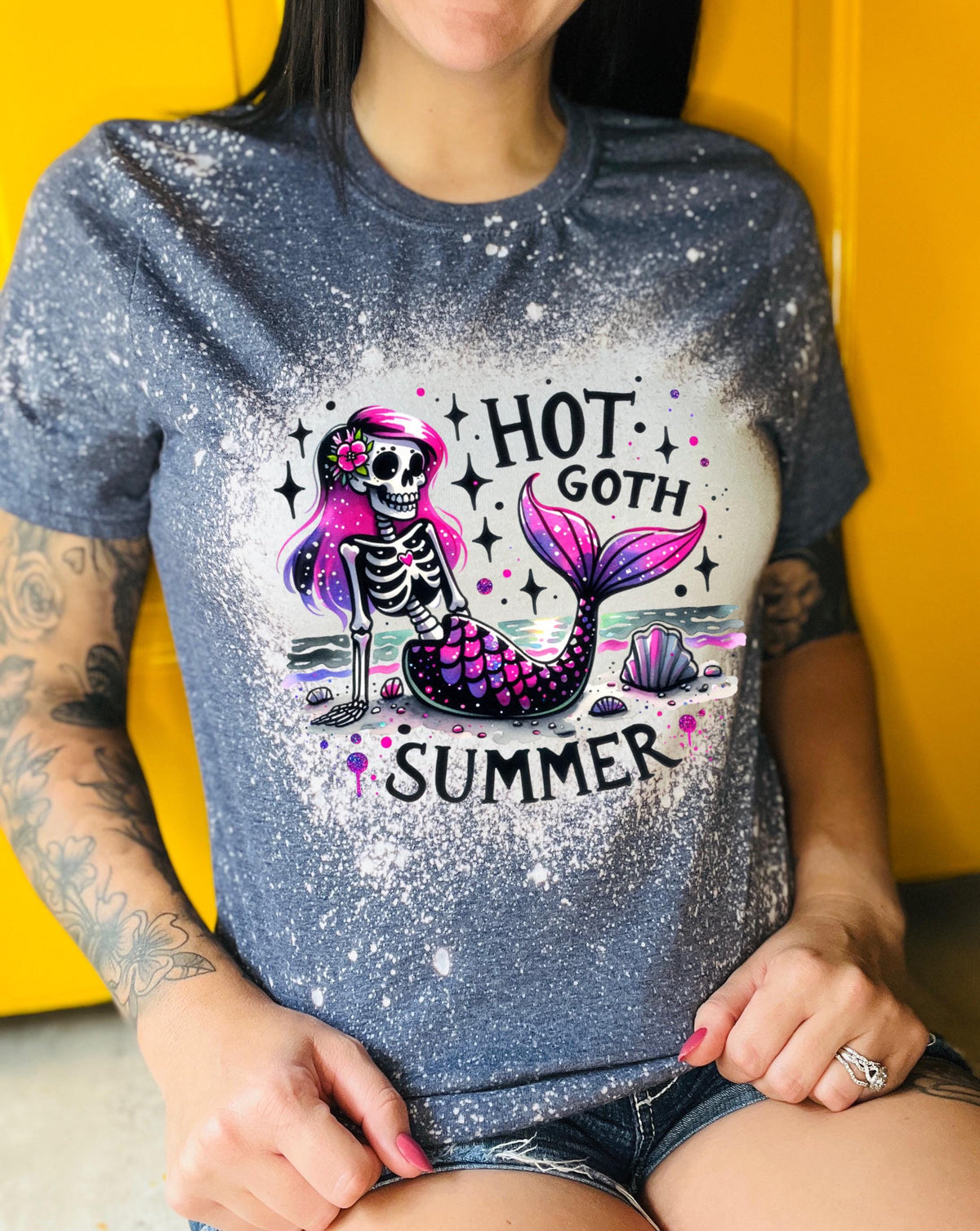 A navy t-shirt with a bleach-splattered design featuring a pink and purple skeleton mermaid with the text "Hot Goth Summer".
