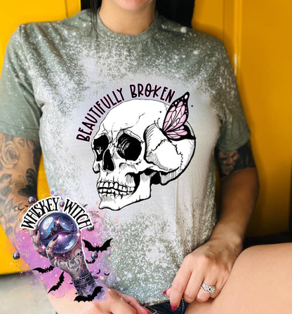 Military Green colored  bleached t-shirt with a white skull and butterfly graphic. The text "Beautifully Broken" is printed above the skull.