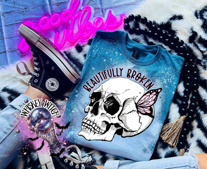 Galapagos Blue bleached t-shirt with a white skull and butterfly graphic. The text "Beautifully Broken" is printed above the skull.