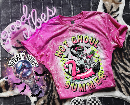 A pink and bleach splattered effect  t-shirt with a graphic of a zombie woman in a flamingo pool float, holding a cocktail. The text "Hot Ghoul Summer" is printed on the shirt.