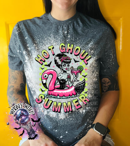 A grey and bleach splattered effect  t-shirt with a graphic of a zombie woman in a flamingo pool float, holding a cocktail. The text "Hot Ghoul Summer" is printed on the shirt.