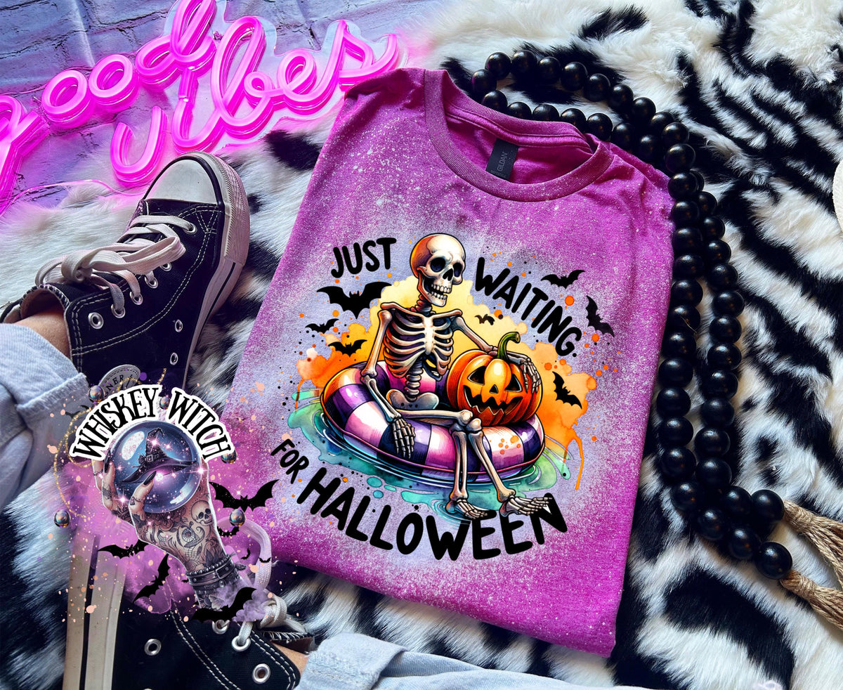 Berry Pink t-shirt with a bleached effect featuring a skeleton sitting in a pool float with a pumpkin. The text on the shirt reads "Just Waiting for Halloween".