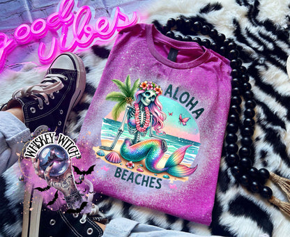 A Berry pink t-shirt with a bleached effect features a colorful skeleton mermaid with a flower crown, palm tree, and seashells. The text "Aloha Beaches" is printed on the shirt.