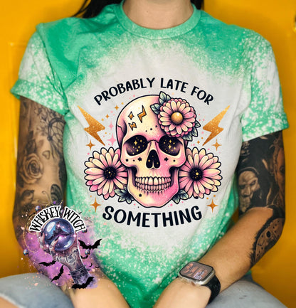 A green t-shirt with a bleached effect featuring a skull with flowers and the text "Probably Late For Something" in gold glitter.