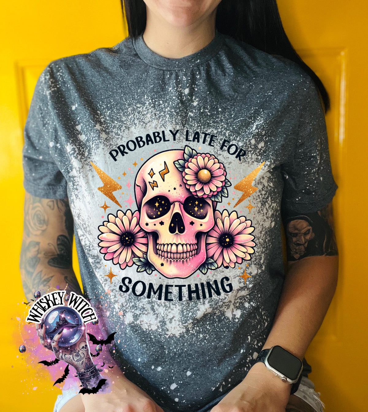 A grey t-shirt with a bleached effect featuring a skull with flowers and the text "Probably Late For Something" in gold glitter.