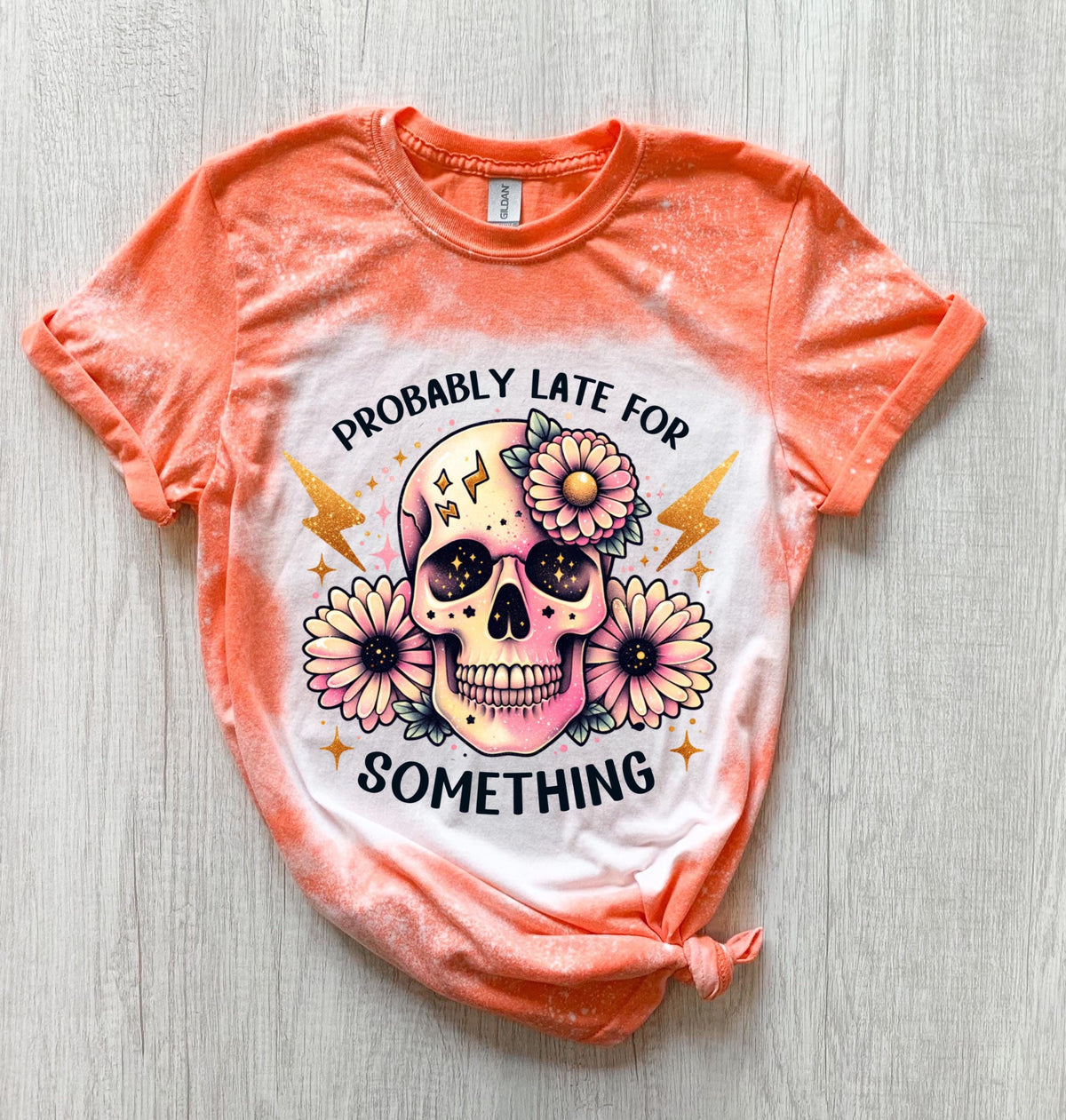 A Orange  t-shirt with a bleached effect featuring a skull with flowers and the text "Probably Late For Something" in gold glitter.