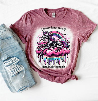 A maroon  and bleached design T shirt with a skeleton unicorn and a rainbow with a dripping colored cloud with the words “Therapy is not enough, I need to bite people.”