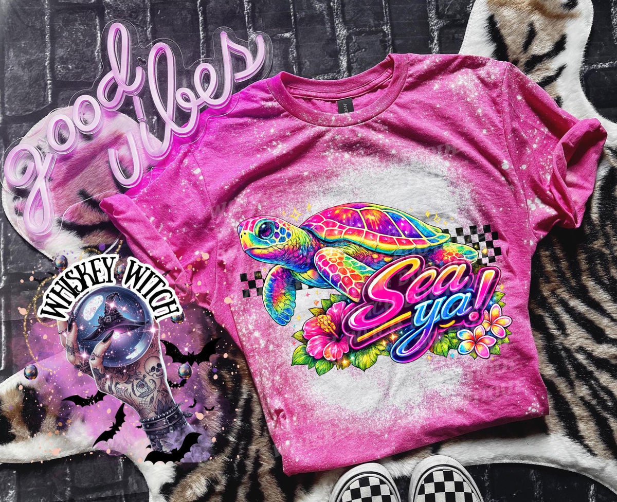 A pink t-shirt with bleach white effect a colorful graphic of a sea turtle, flowers, and the words "Sea Ya!". The shirt has a bleached, distressed look. The design features vibrant colors and a playful font.