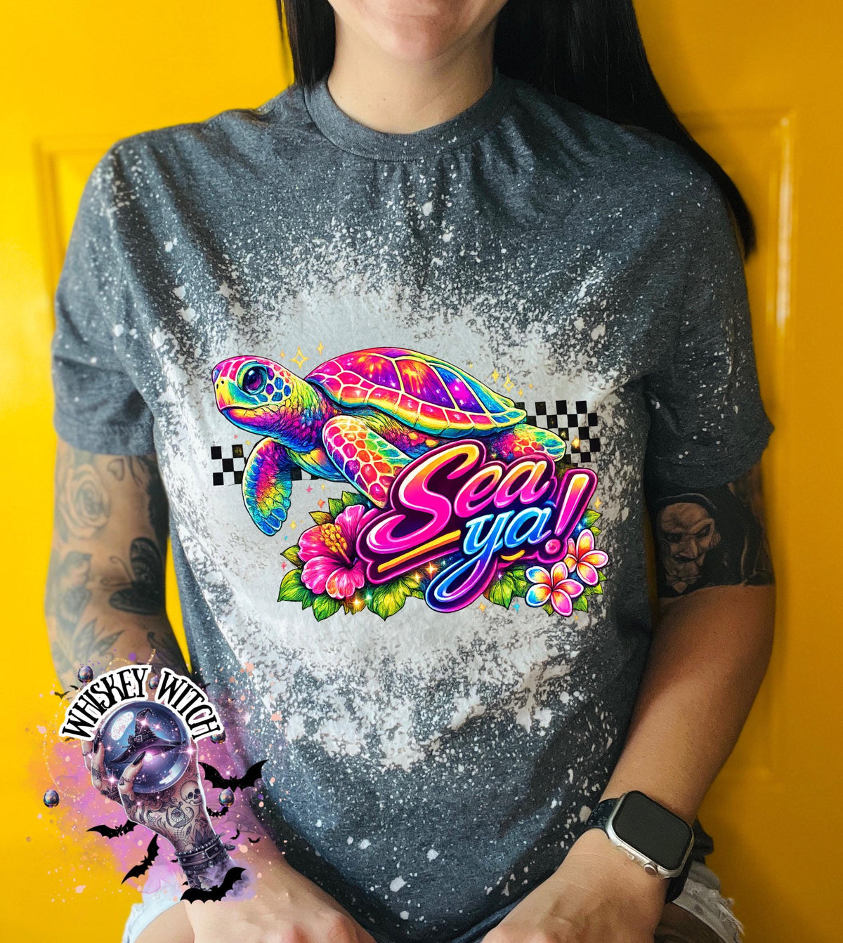 A grey t-shirt with bleach white effect a colorful graphic of a sea turtle, flowers, and the words "Sea Ya!". The shirt has a bleached, distressed look. The design features vibrant colors and a playful font.