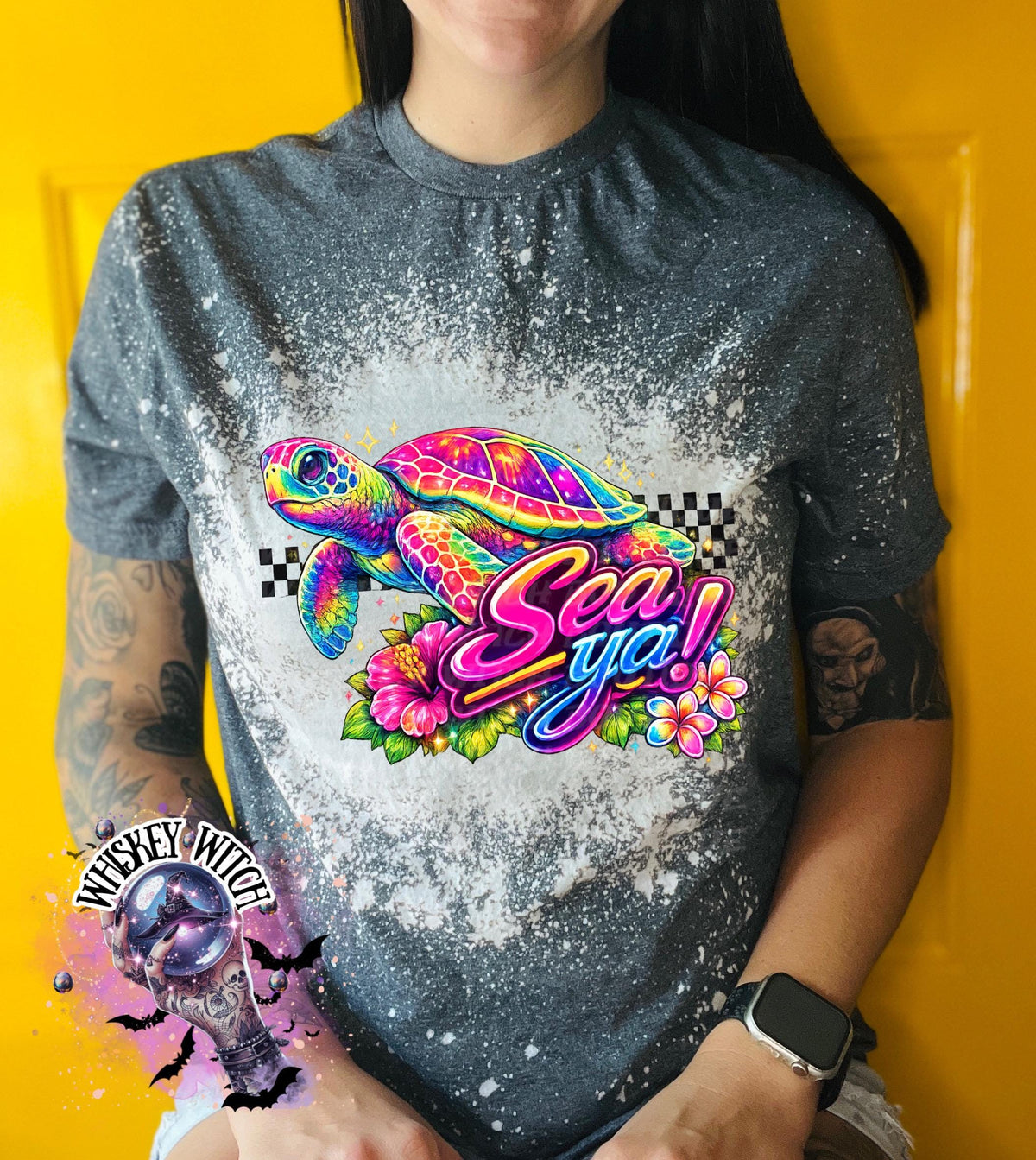 A grey t-shirt with bleach white effect a colorful graphic of a sea turtle, flowers, and the words "Sea Ya!". The shirt has a bleached, distressed look. The design features vibrant colors and a playful font.