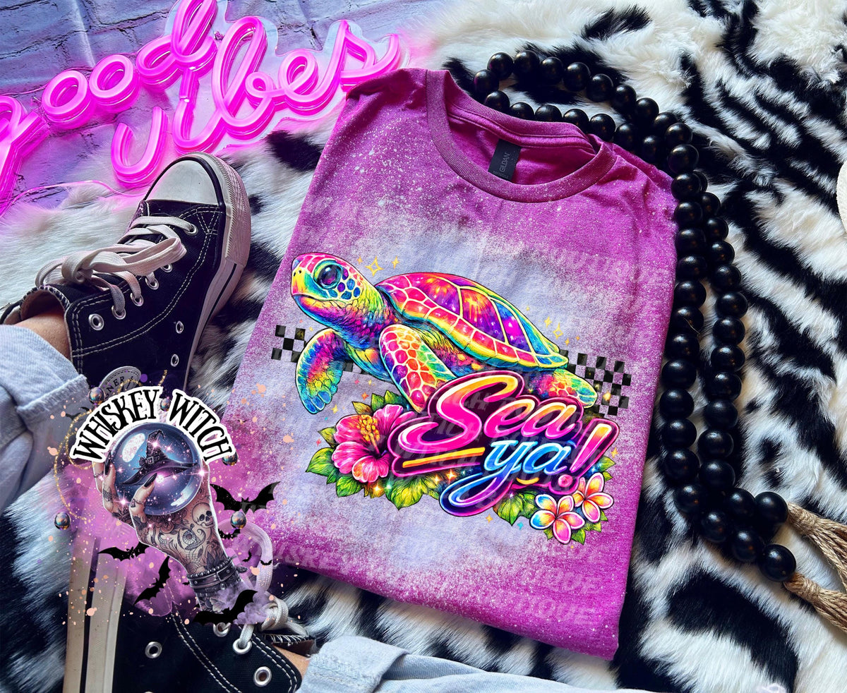 A Berry pink  t-shirt with bleach white effect a colorful graphic of a sea turtle, flowers, and the words "Sea Ya!". The shirt has a bleached, distressed look. The design features vibrant colors and a playful font.