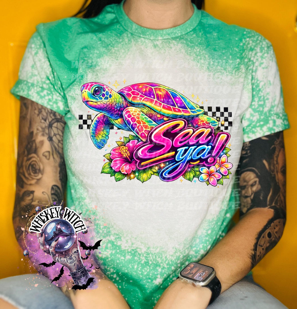 A green t-shirt with bleach white effect a colorful graphic of a sea turtle, flowers, and the words "Sea Ya!". The shirt has a bleached, distressed look. The design features vibrant colors and a playful font.