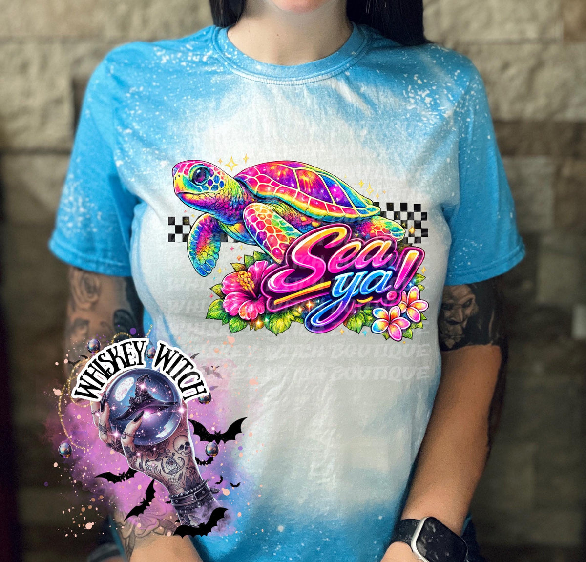 A saphire blue t-shirt with bleach white effect a colorful graphic of a sea turtle, flowers, and the words "Sea Ya!". The shirt has a bleached, distressed look. The design features vibrant colors and a playful font.
