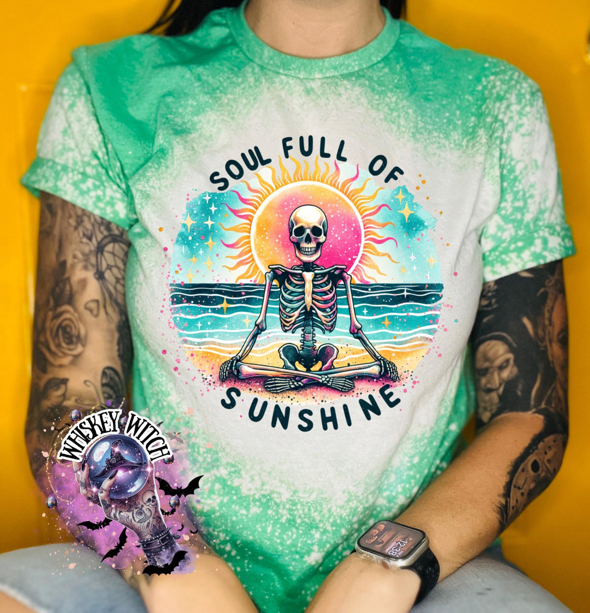 A green and bleach white splatter  t-shirt featuring a skeleton meditating on a beach with a sun in the background. The text on the shirt reads "SOUL FULL OF SUNSHINE".