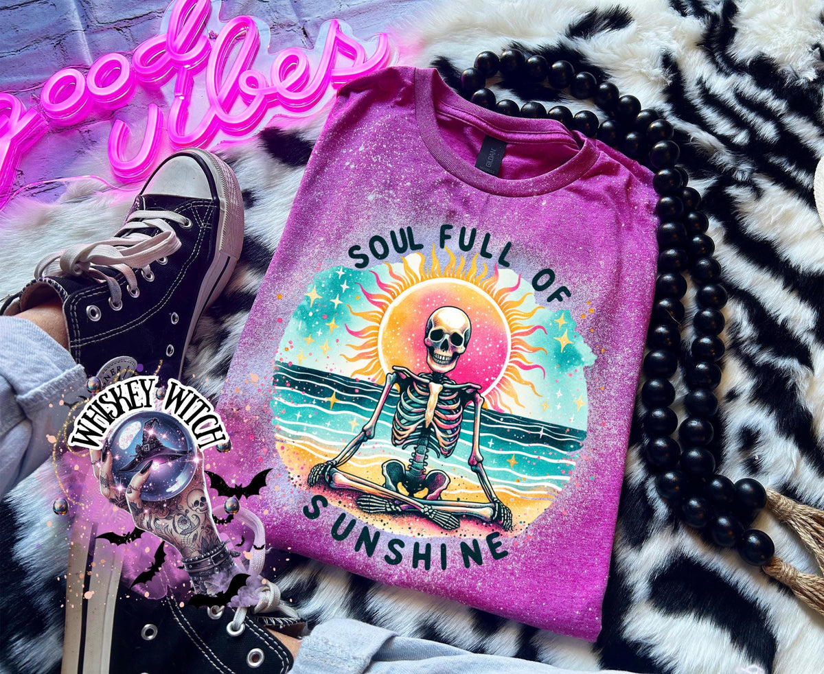 A Berry pink  and bleach white splatter  t-shirt featuring a skeleton meditating on a beach with a sun in the background. The text on the shirt reads "SOUL FULL OF SUNSHINE".