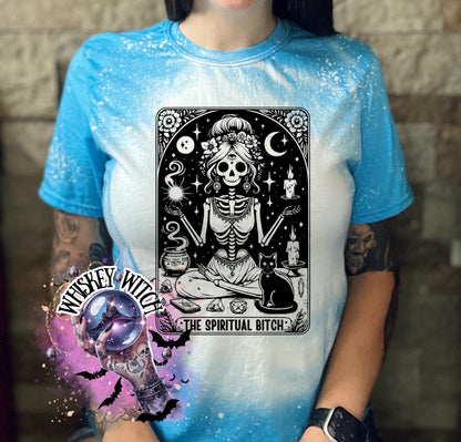 A bleached saphire blue t-shirt with a black and white illustration of a skeleton woman with a cat and the text "The Spiritual Bitch".