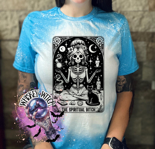 A bleached saphire blue t-shirt with a black and white illustration of a skeleton woman with a cat and the text "The Spiritual Bitch".