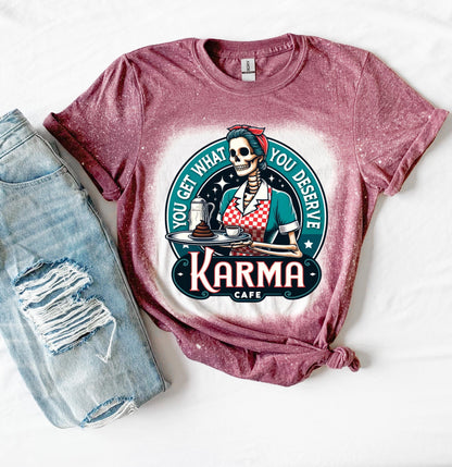 A maroon t-shirt with a bleached design featuring a skeleton wearing a red and white dress and holding a tray with a cup of coffee and a piece of cake. The text "You get what you deserve" is written around the skeleton. Below the skeleton is the text "Karma Cafe".