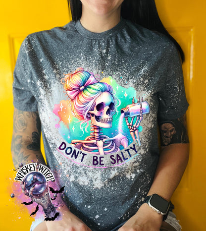 A dark Heather  t-shirt with a bleached effect featuring a skeleton with rainbow hair pouring salt from a shaker. The text "Don't Be Salty" is printed on the shirt