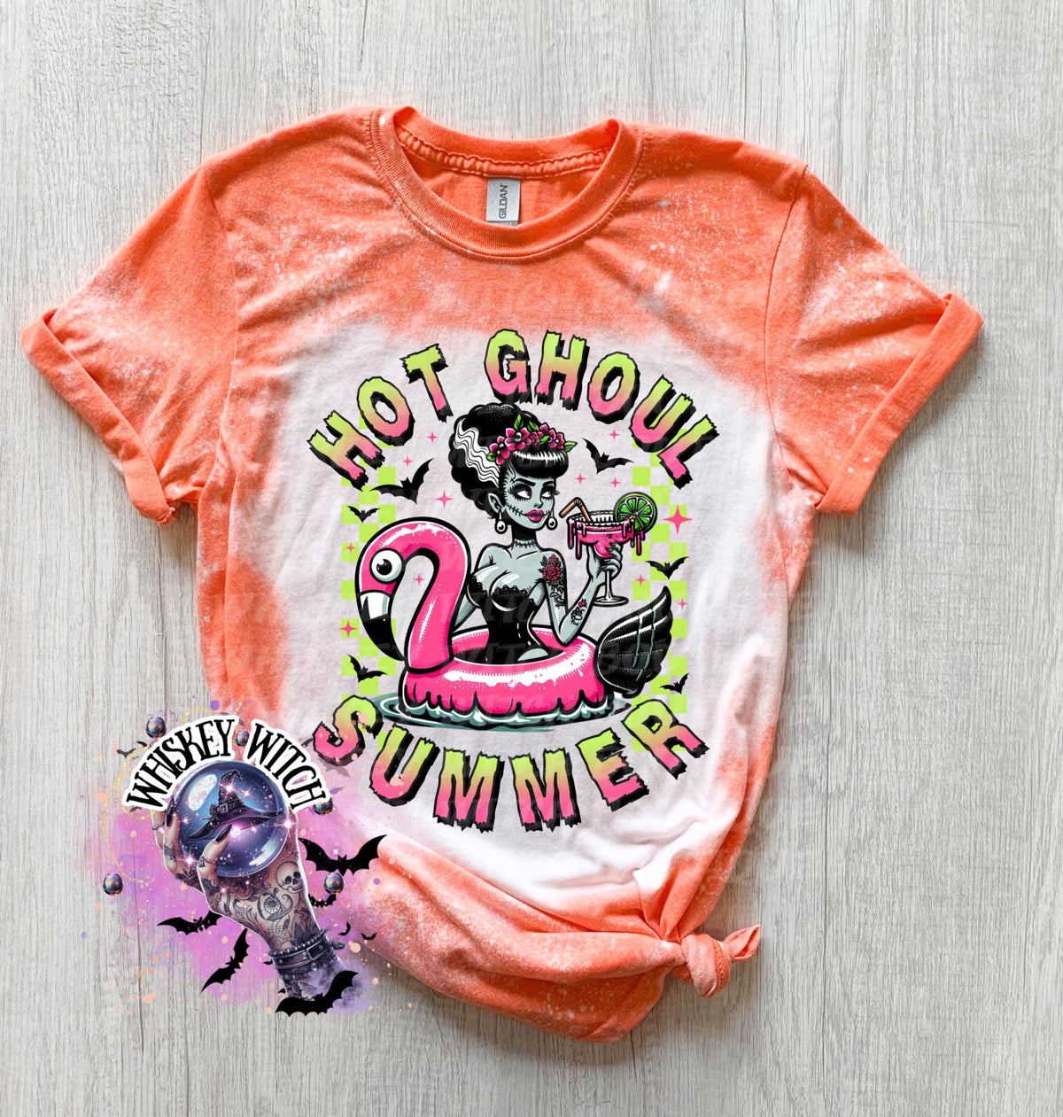 A Orange and bleach splattered effect  t-shirt with a graphic of a zombie woman in a flamingo pool float, holding a cocktail. The text "Hot Ghoul Summer" is printed on the shirt.