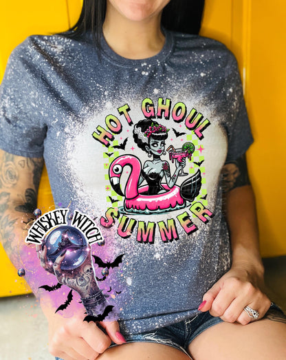 A navy blue  and bleach splattered effect  t-shirt with a graphic of a zombie woman in a flamingo pool float, holding a cocktail. The text "Hot Ghoul Summer" is printed on the shirt.