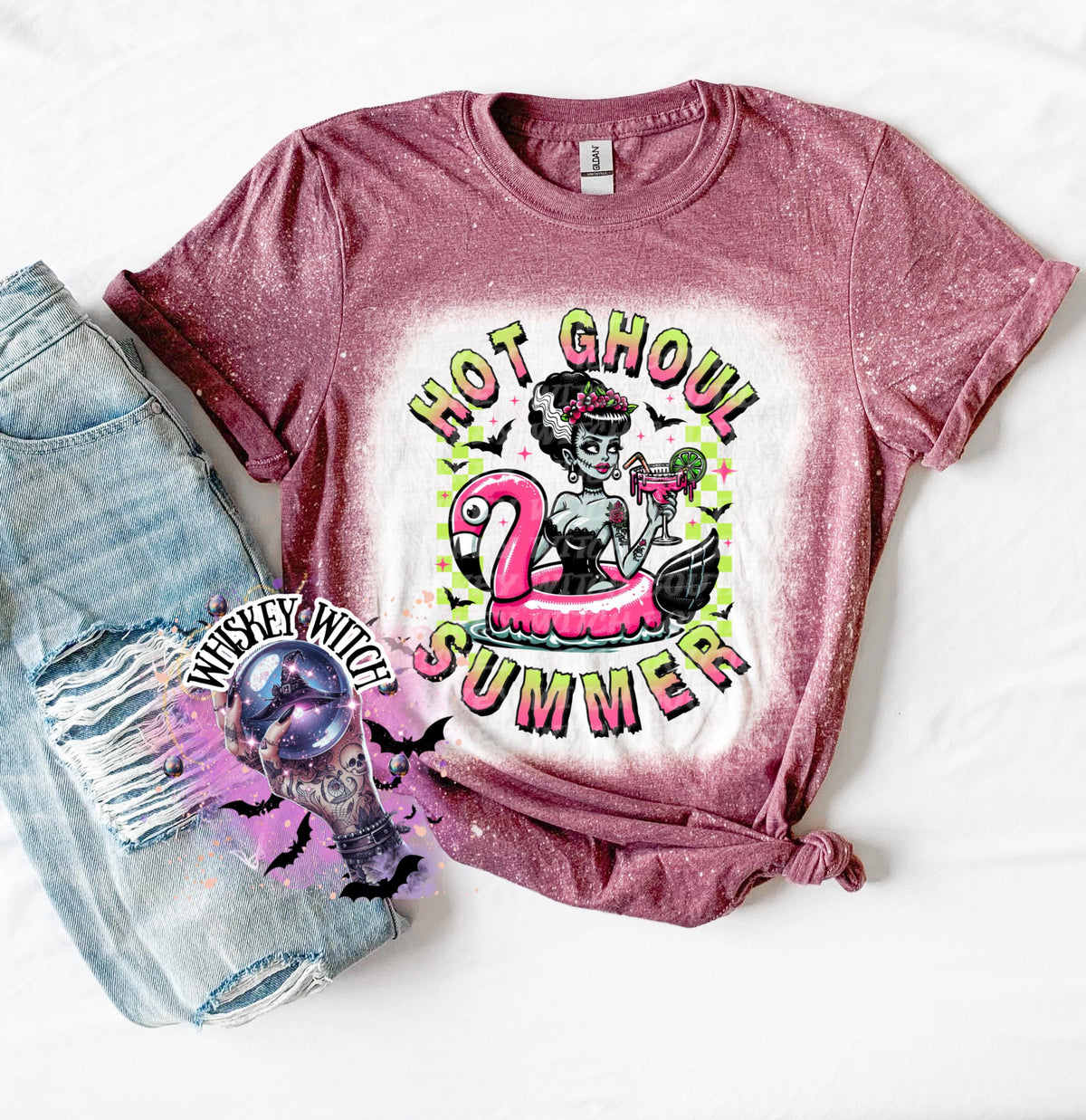 A maroon and bleach splattered effect  t-shirt with a graphic of a zombie woman in a flamingo pool float, holding a cocktail. The text "Hot Ghoul Summer" is printed on the shirt.