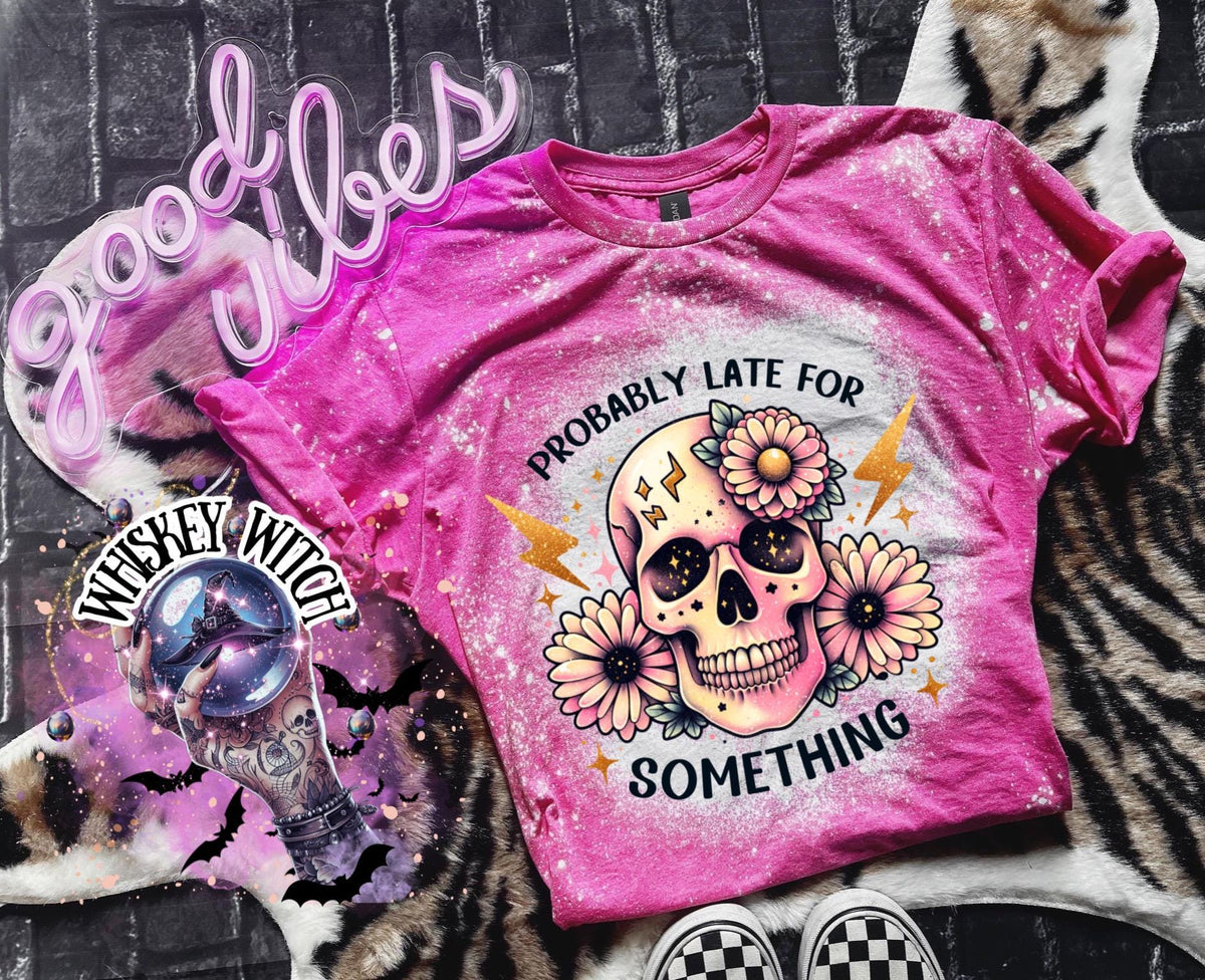 A pink  t-shirt with a bleached effect featuring a skull with flowers and the text "Probably Late For Something" in gold glitter.
