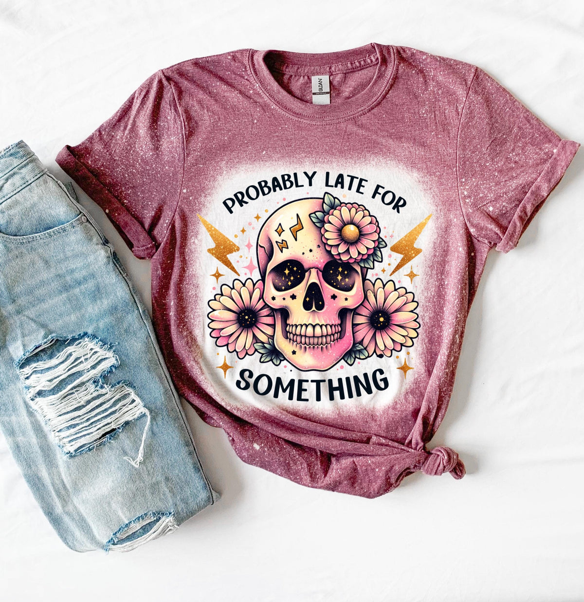 A maroon t-shirt with a bleached effect featuring a skull with flowers and the text "Probably Late For Something" in gold glitter.