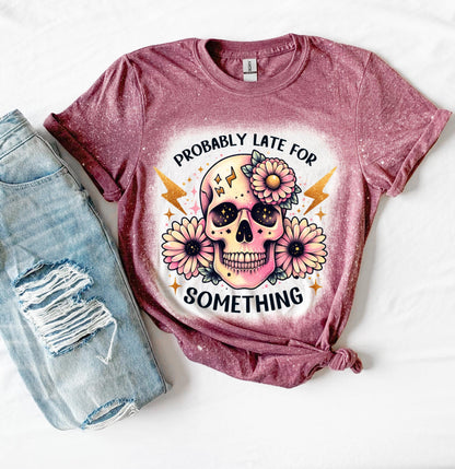 A maroon t-shirt with a bleached effect featuring a skull with flowers and the text "Probably Late For Something" in gold glitter.