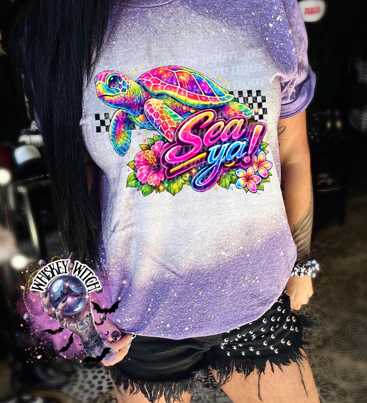 A purple t-shirt with bleach white effect a colorful graphic of a sea turtle, flowers, and the words "Sea Ya!". The shirt has a bleached, distressed look. The design features vibrant colors and a playful font.