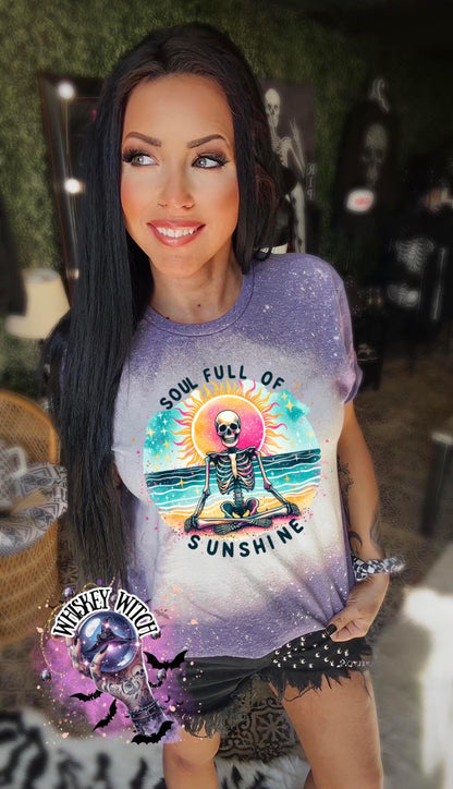 A purple  and bleach white splatter  t-shirt featuring a skeleton meditating on a beach with a sun in the background. The text on the shirt reads "SOUL FULL OF SUNSHINE".
