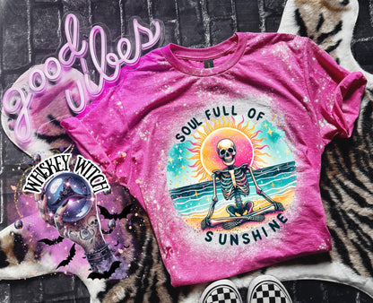 A pink and bleach white splatter  t-shirt featuring a skeleton meditating on a beach with a sun in the background. The text on the shirt reads "SOUL FULL OF SUNSHINE".