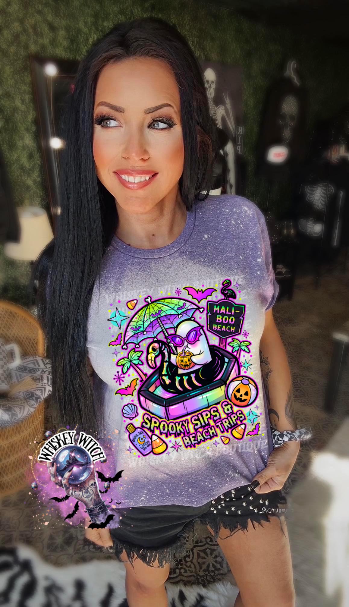 Close-up of spooky beach shirt design with ghost in float, tropical palm trees, bats, candy corn, and neon summer colors.