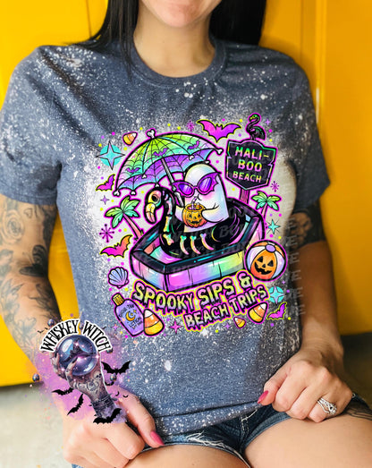 Close-up of spooky beach shirt design with ghost in float, tropical palm trees, bats, candy corn, and neon summer colors.
