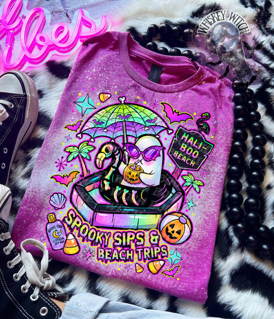Close-up of spooky beach shirt design with ghost in float, tropical palm trees, bats, candy corn, and neon summer colors.