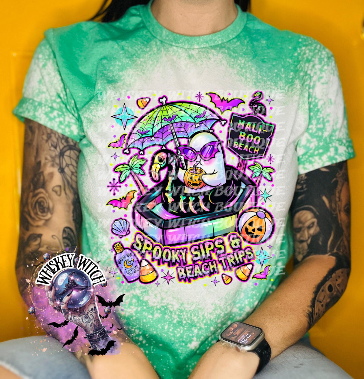 Close-up of spooky beach shirt design with ghost in float, tropical palm trees, bats, candy corn, and neon summer colors.