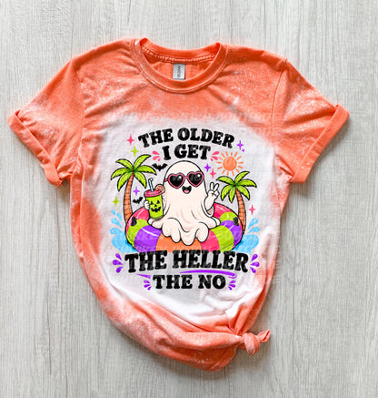 Orange and white tie-dye t-shirt with a graphic of a ghost wearing sunglasses and floating on an inner tube. The text reads "THE OLDER I GET THE HELLER THE NO". The ghost is holding a drink.